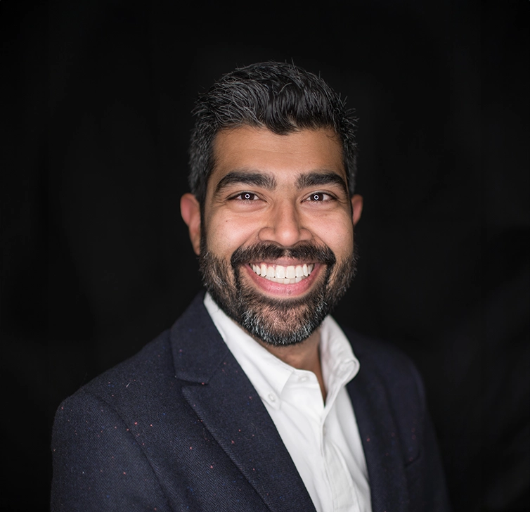 Smiling person in a suit against a black background.